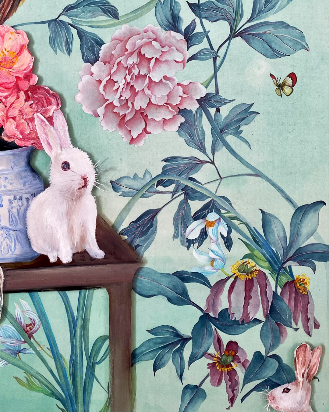 A decorative art print or wallpaper design featuring a white rabbit sitting on a wooden table next to pink peonies, with blue-green foliage, a butterfly, and additional rabbits on a light aqua background.
