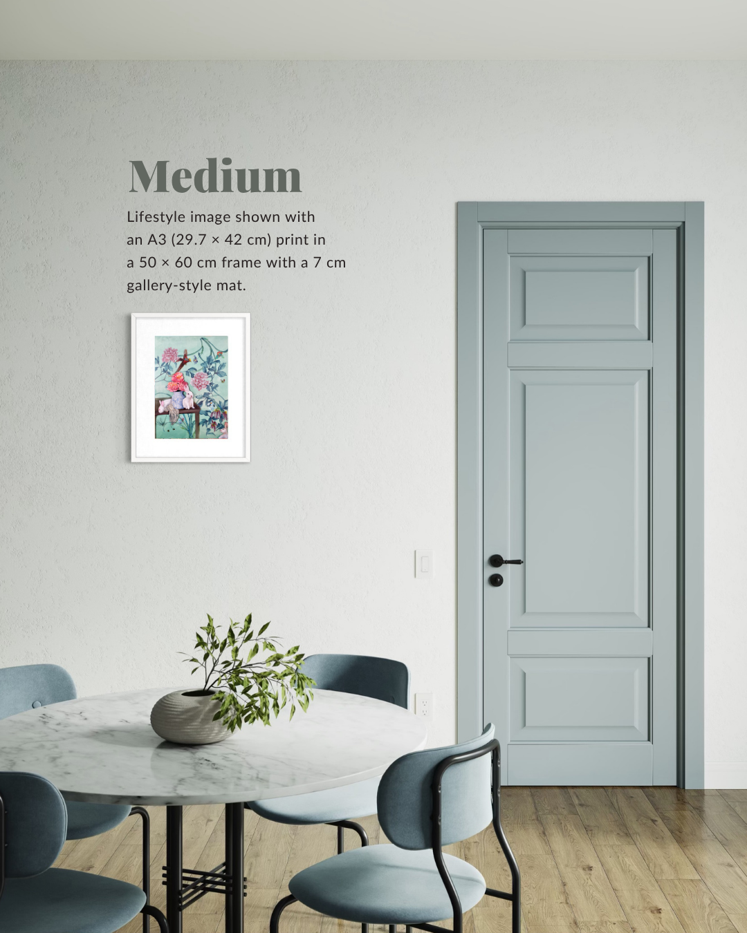 A framed art print displayed on a light gray wall in a dining room setting, with text reading 'Medium' and describing the print size and presentation. A pale blue paneled door and matching chairs are visible in the background.