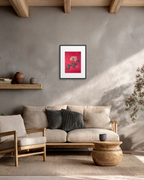 A framed art print featuring a vibrant red background with a pink and green floral design, displayed on a textured gray wall above a beige sofa in a modern, rustic living room setting.