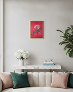 A framed art print featuring a pink rose with green leaves on a vibrant pink background, displayed on a light gray wall above a marble console table with decorative pillows and a vase of white flowers.