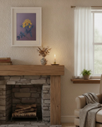 A cozy living room scene featuring a stone fireplace with a rustic wooden mantel, a framed floral print on the wall, a lit candle, and a window with sheer white curtains.