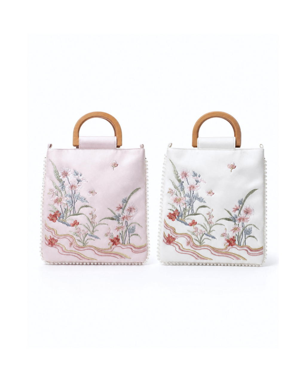 Two small structured handbags with light wood top handles, shown side by side on a white background. The left bag is pale pink with floral embroidery, and the right bag is white with matching floral embroidery.