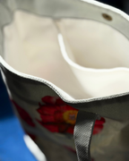 Close-up of the interior opening of a canvas tote bag, showing a cream-colored inner lining and a gray fabric exterior with a red floral print and gray webbing handles.