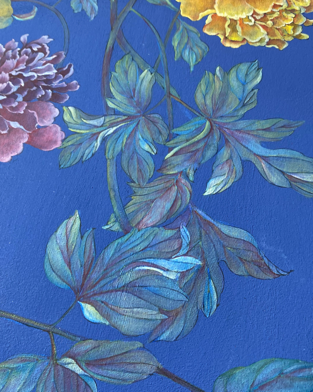 A close-up of a floral painting featuring blue-green leaves and stems against a rich blue background, with partial pink and yellow flowers visible at the edges.