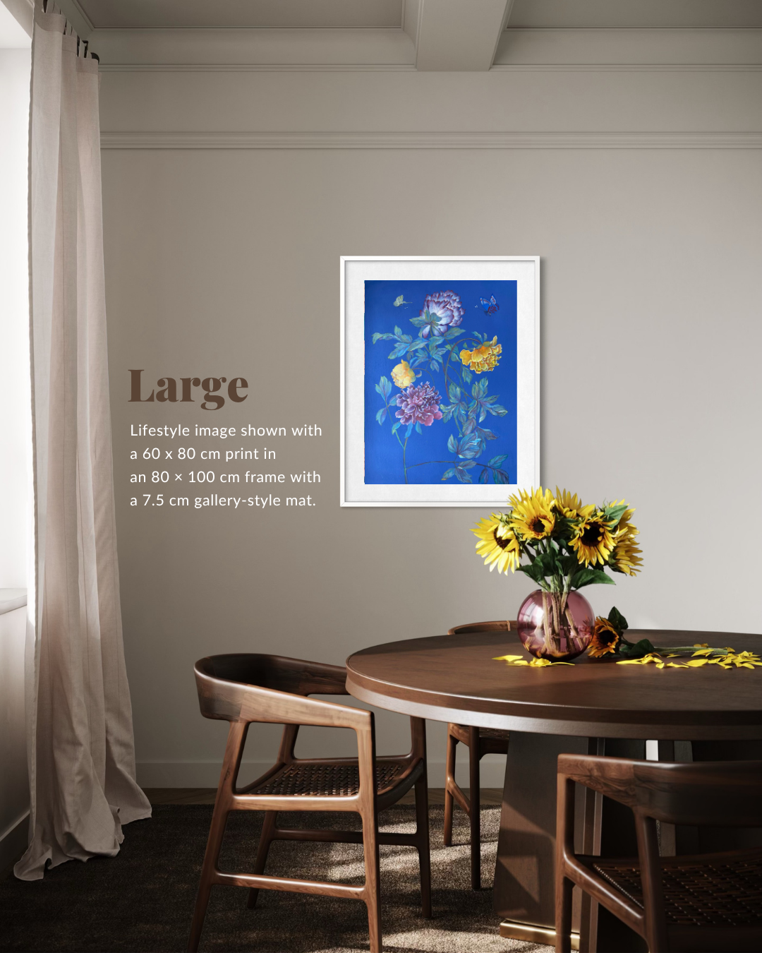 A framed floral art print with a vivid blue background and multicolored flowers hangs on a beige wall in a dining room setting with a wooden table, chairs, and a vase of sunflowers. Text on the left reads 'Large Lifestyle image shown with a 60 x 80 cm print in an 80 x 100 cm frame with a 7.