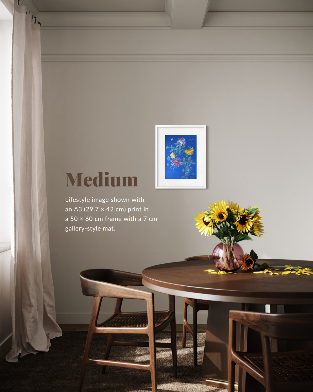 A framed art print featuring a blue floral scene hangs on a light gray wall in a dining room setting with a wooden table, chairs, and a vase of yellow sunflowers. Text on the left reads 'Medium' with additional sizing information.