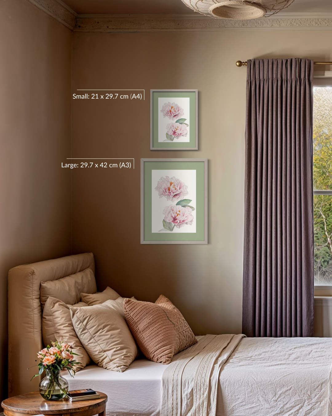 A styled bedroom interior showing two framed floral wall art prints hanging above a bed. The prints feature soft pink flowers with green leaves in light green frames.