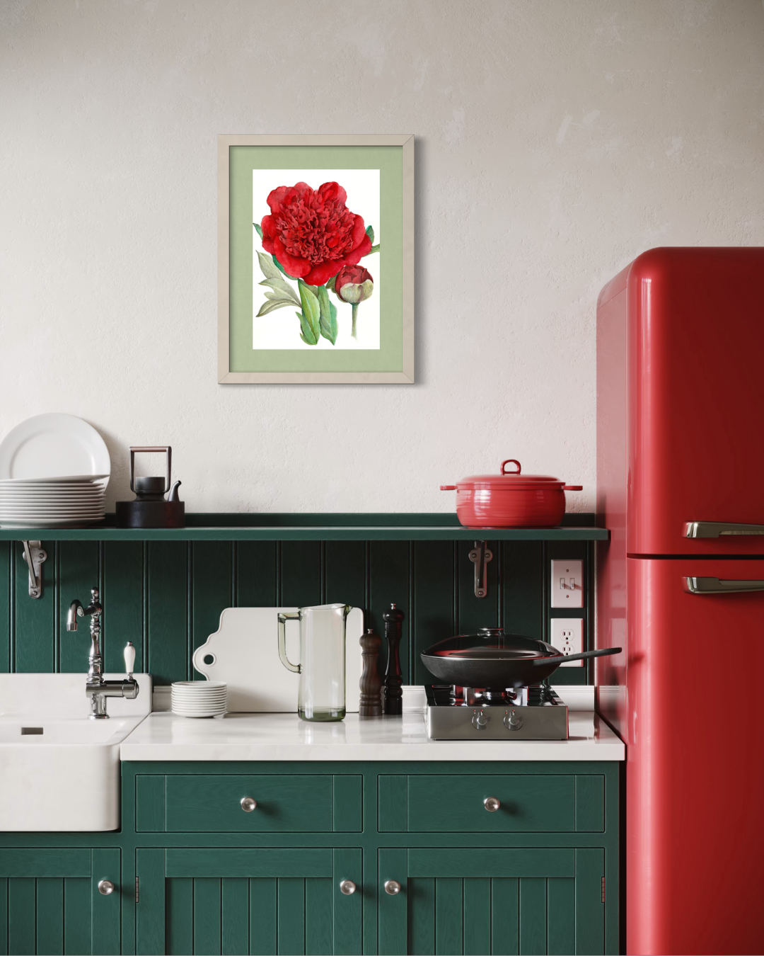A framed botanical art print of a red peony with green leaves, displayed on a textured off-white wall above a dark green kitchen counter with a white sink and a red refrigerator.