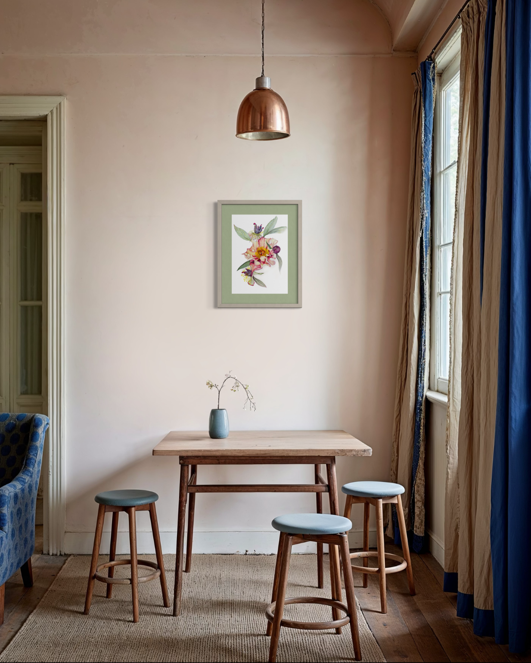 A styled interior scene with a small wooden table, three wooden stools with blue-gray cushions, a copper pendant light, beige walls, blue curtains, and a framed floral print on the wall.