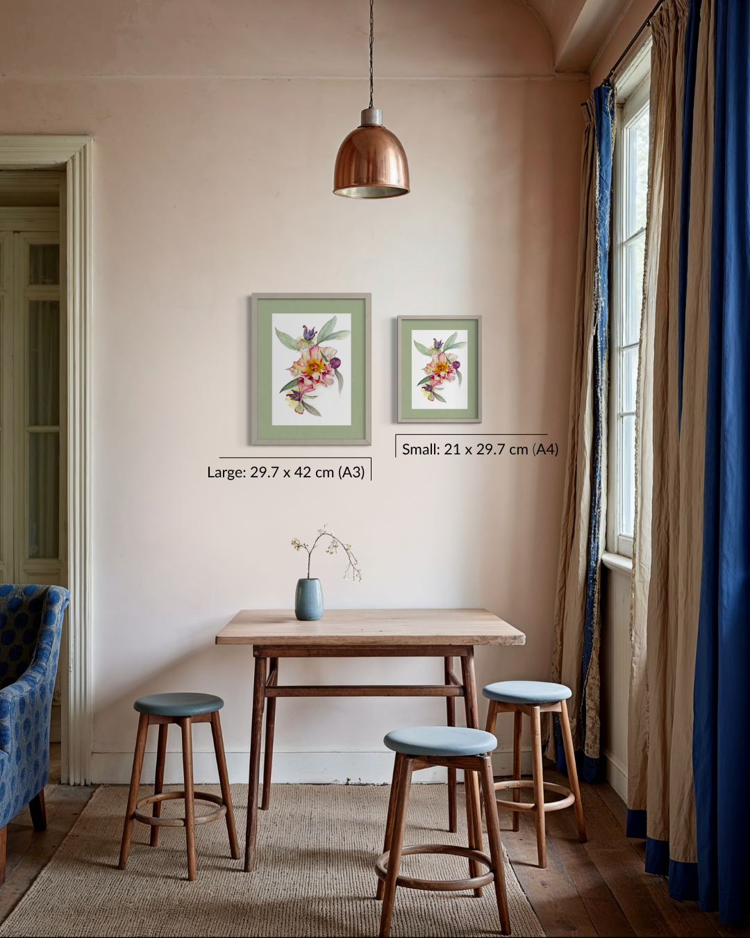 A styled interior room showing two framed botanical art prints on a beige wall above a small wooden table and stools. The prints are labeled as large 29.