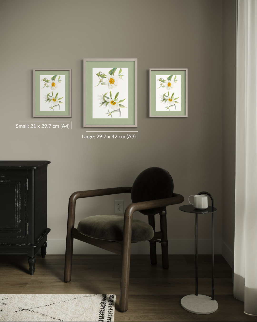 Three framed botanical art prints with yellow flowers and green leaves are displayed on a taupe-gray wall above a dark wood armchair, with size labels for Small (A4) and Large (A3) versions. A black side table with a white mug sits to the right.