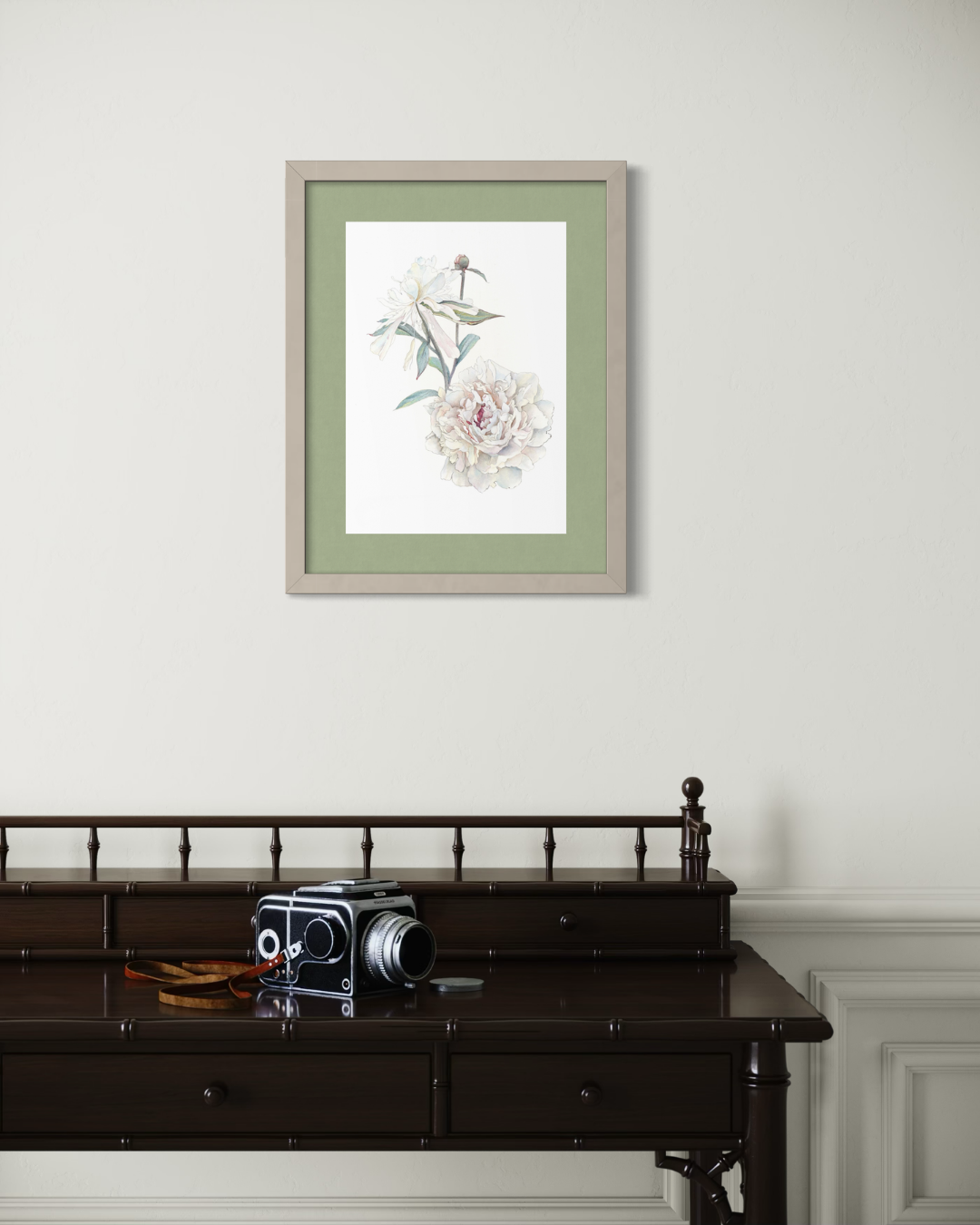 A framed botanical art print featuring a white peony and a small bird, styled on a light gray wall above a dark wooden console table with a vintage camera.