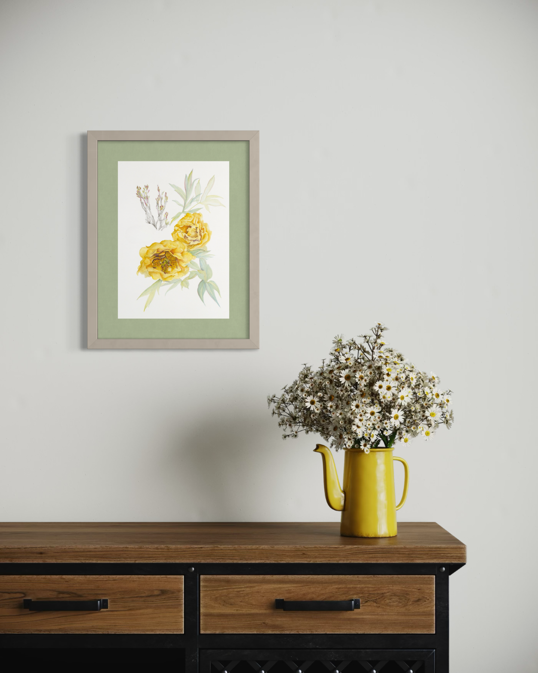 Framed botanical wall art featuring yellow flowers and green leaves, displayed on a light gray wall above a wooden console table with a yellow pitcher of dried flowers.