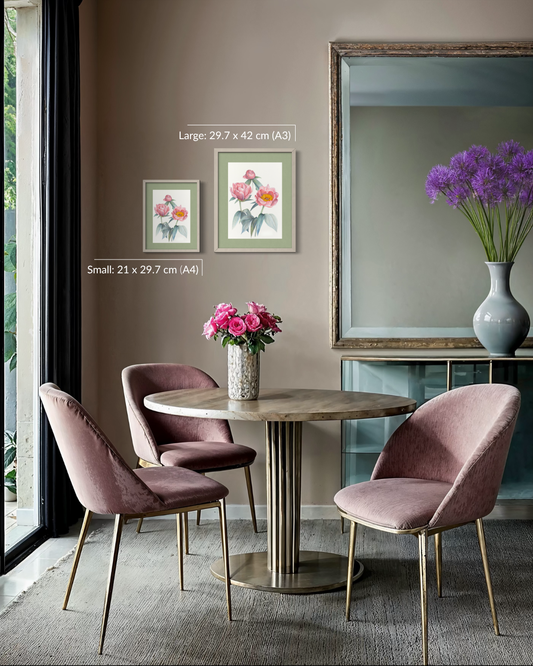 A styled dining room scene featuring a round wooden table with a fluted pedestal base, surrounded by three blush pink velvet chairs with gold legs. A large mirror on the wall reflects a vase of purple flowers, and two framed floral prints are mounted on the taupe wall.