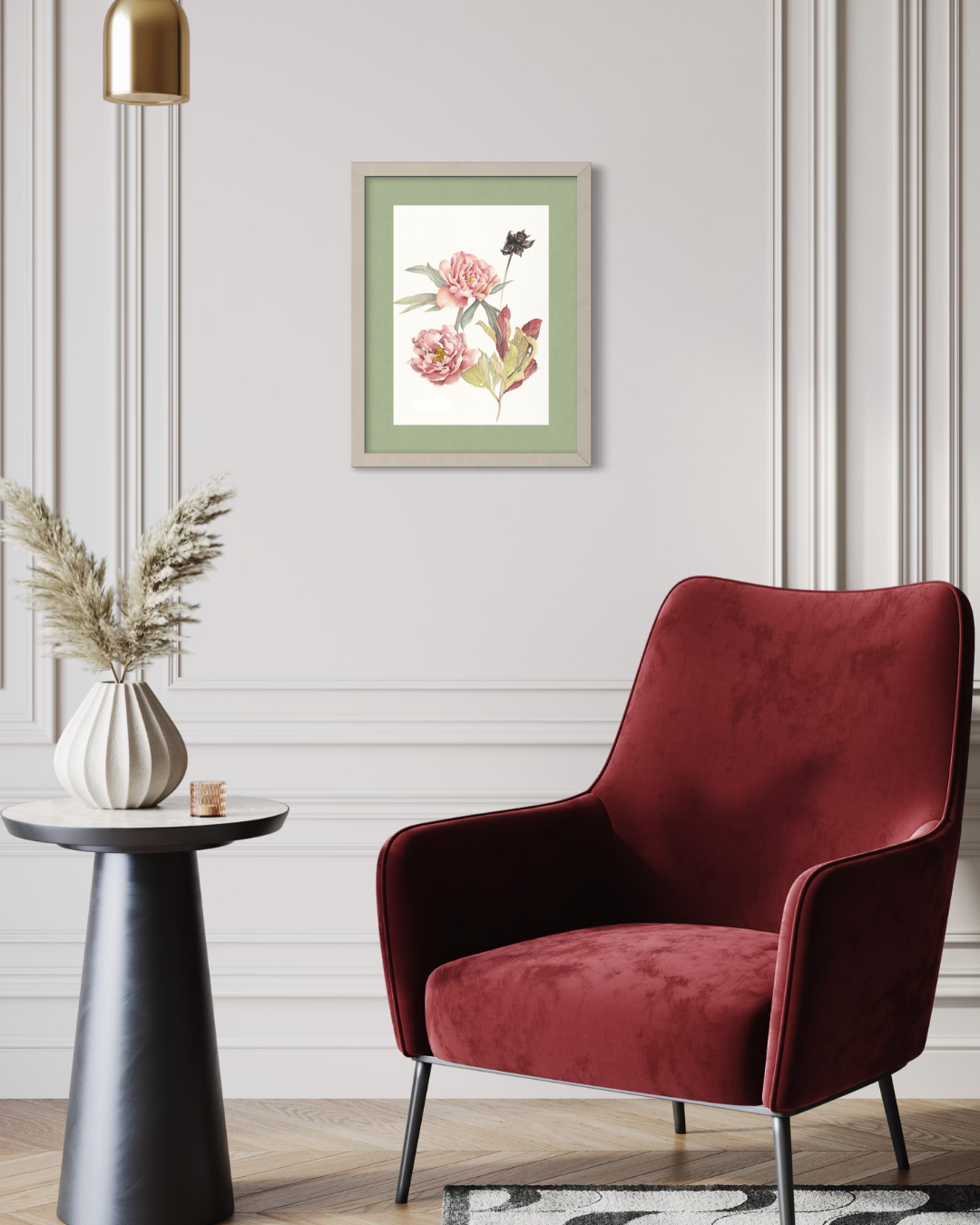 A framed botanical art print featuring pink flowers and green leaves, styled in a modern living room setting above a deep red velvet armchair and next to a side table with a vase of dried grass.