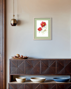 A framed art print featuring two red flowers with green leaves, displayed on a light beige wall above a dark wood console table with decorative bowls.