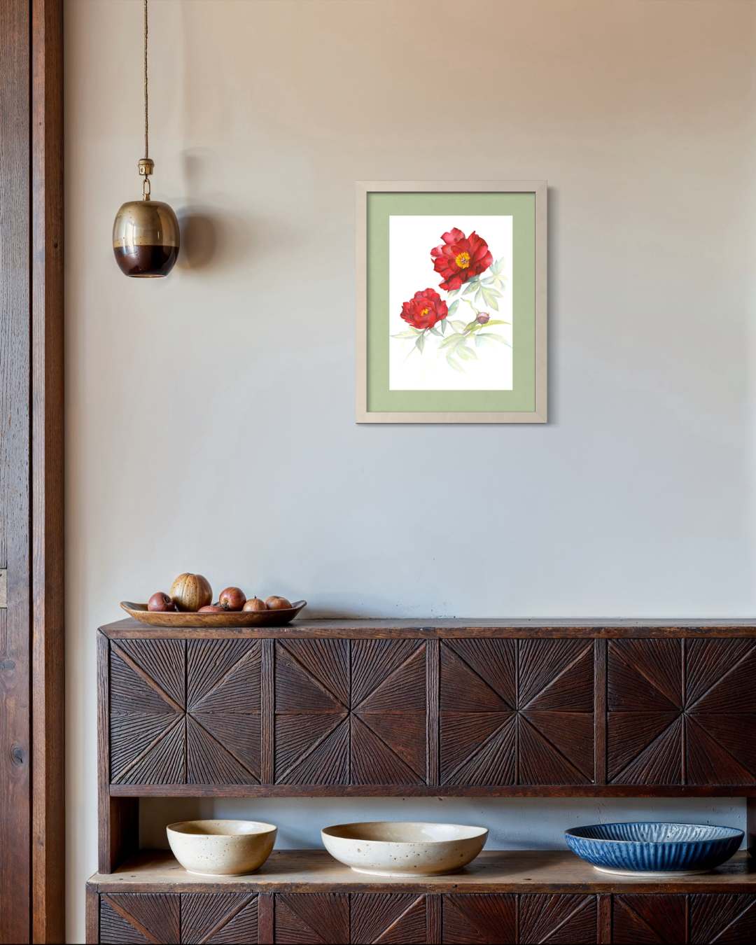 A framed art print featuring two red flowers with green leaves, displayed on a light beige wall above a dark wood console table with decorative bowls.