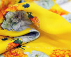 Close-up of a yellow silk scarf with floral patterns, displaying vibrant colors and a luxurious texture.