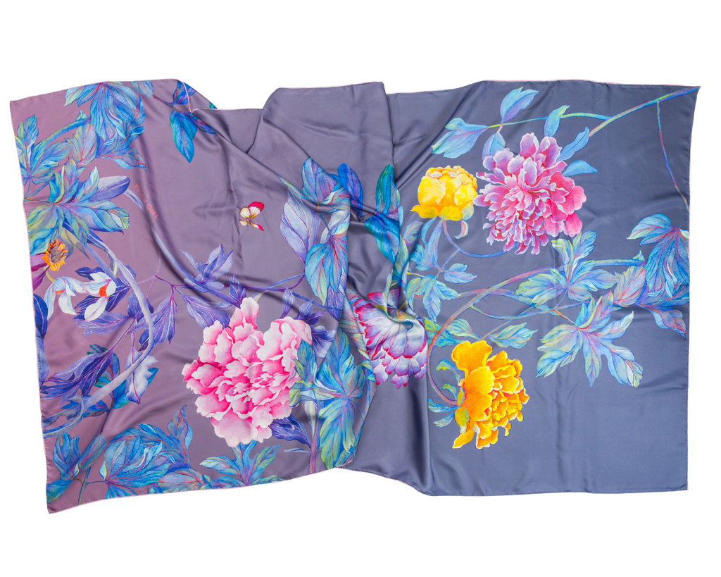 A draped silk scarf featuring a vibrant floral print with pink peonies, yellow flowers, and blue leaves on a dusty purple and slate blue background.