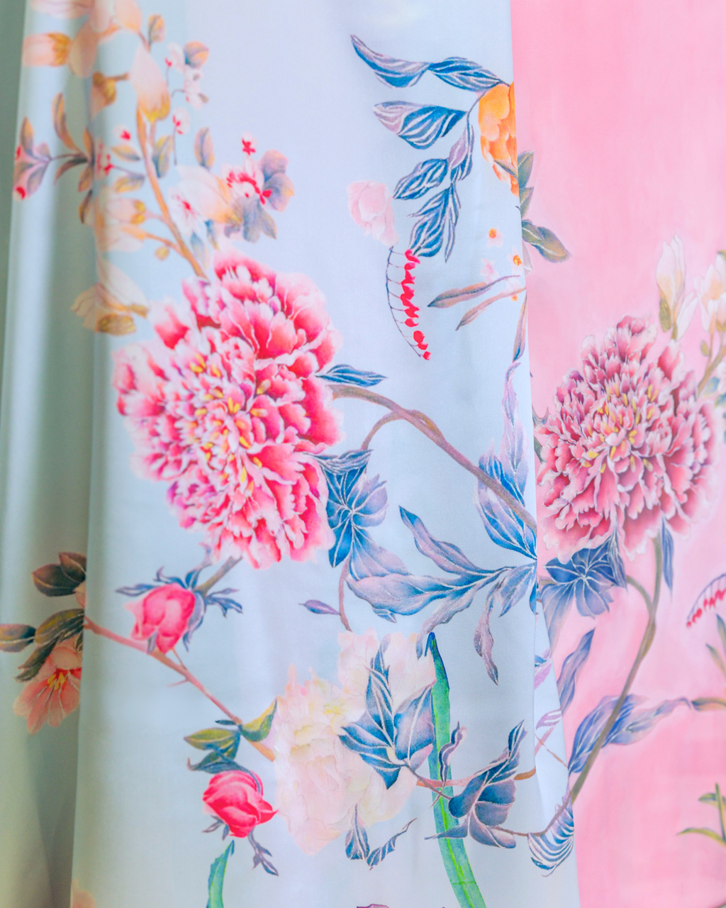 Close-up of a floral fabric print with large pink flowers, blue leaves, and soft pastel background tones, including mint green and pink sections.