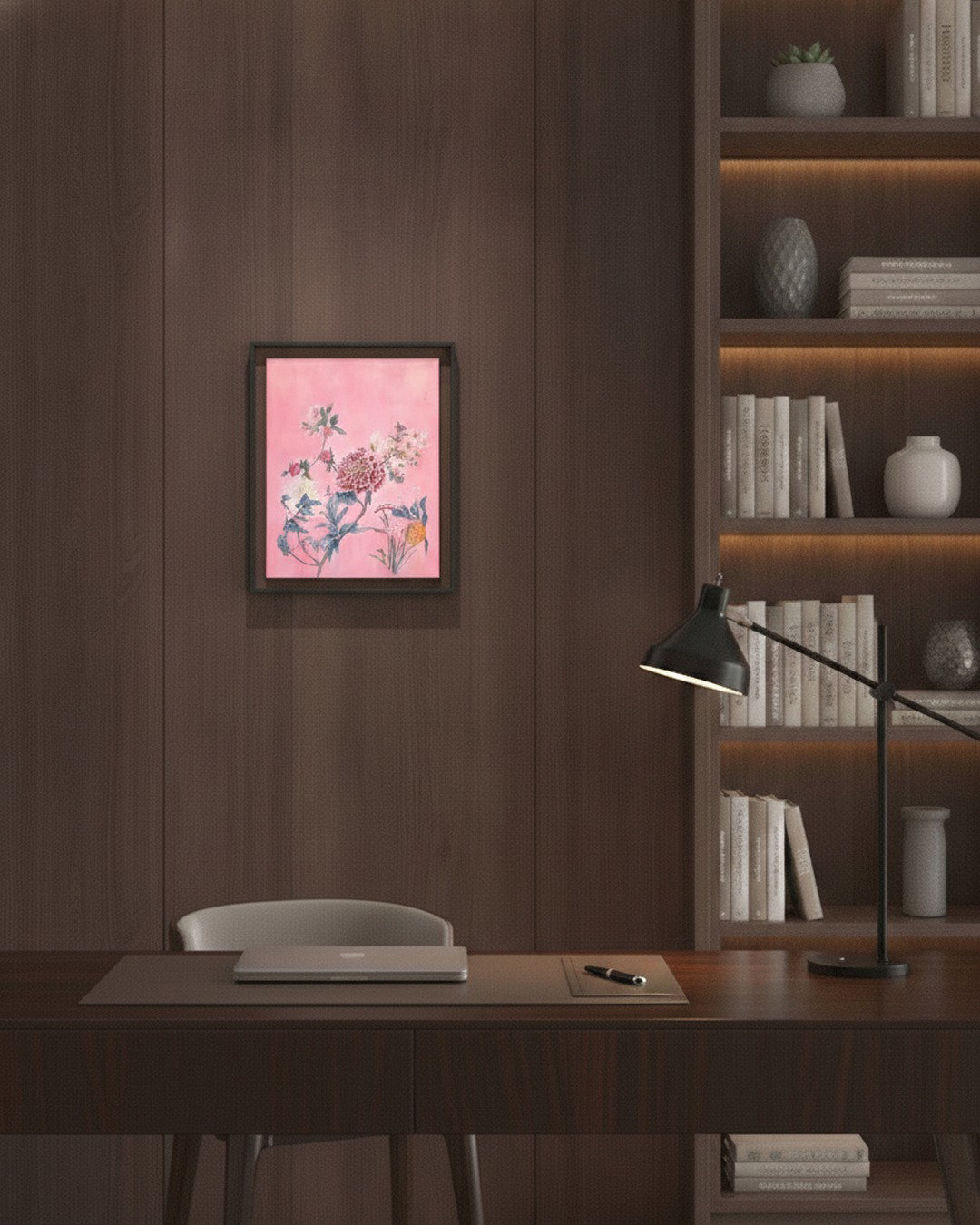 A framed art print featuring a pink background with delicate floral and bird illustrations, displayed on a dark wood wall above a desk in a modern home office setting.