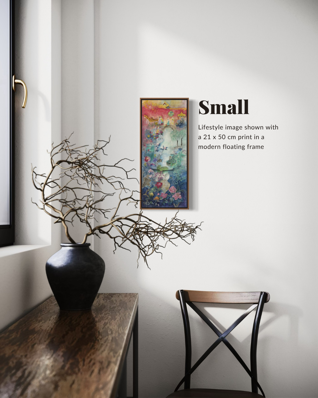 A framed abstract art print labeled 'Small' hangs on a white wall in a styled interior with a dark vase of branches on a wooden table and a chair below. The text notes the print is 21 x 50 cm shown in a modern floating frame.