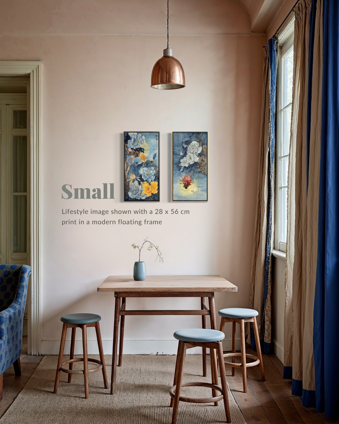 A lifestyle interior scene showing two framed abstract art prints hanging on a beige wall above a small wooden table with three stools. The room has a copper pendant light, blue and beige curtains, and a rug.