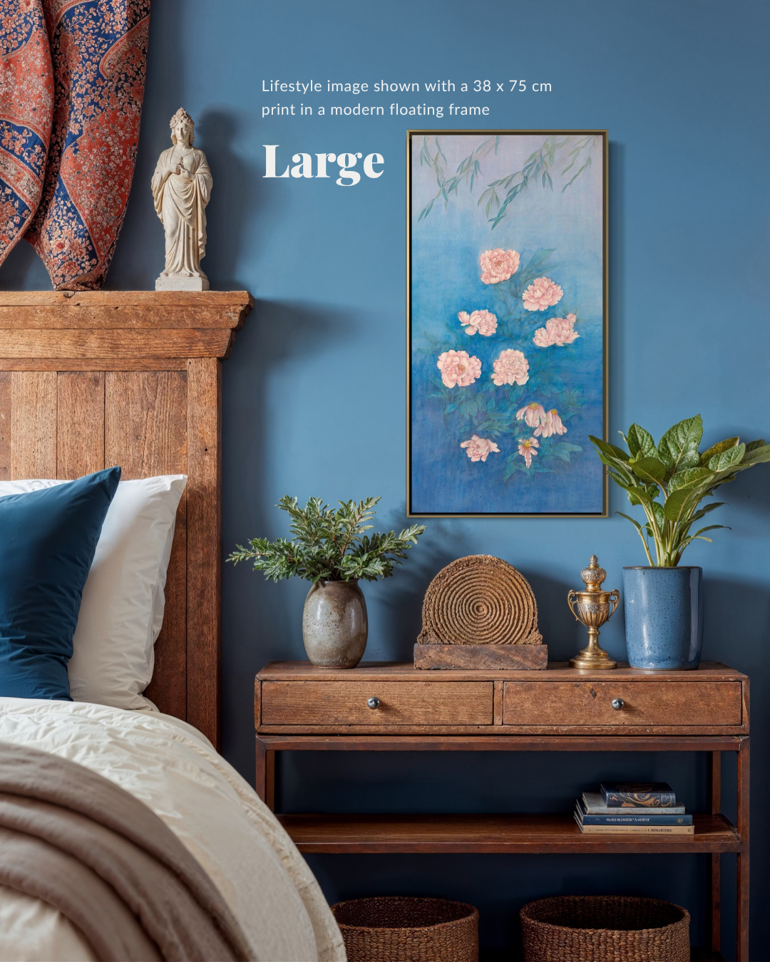 A framed wall art print featuring pink flowers on a blue background, shown hanging in a styled bedroom setting above a wooden console table with plants and decor.