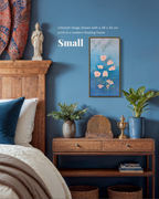 A framed wall art print featuring pink flowers on a blue background, styled in a bedroom setting above a wooden console table. The image includes text reading 'Lifestyle Image shown with a 28 x 54 cm print in a modern floating frame' and 'Small'.